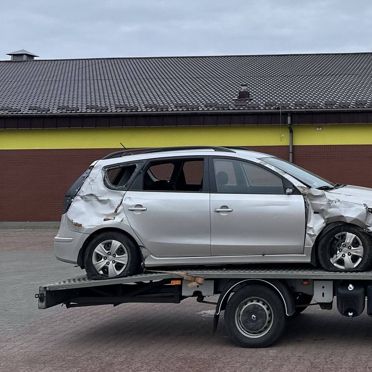 Damaged silver car on a tow truck with visible dents and broken windows.