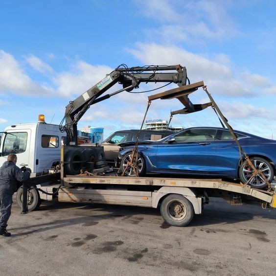 Tow truck with a crane loading a blue car onto its platform in a parking area.