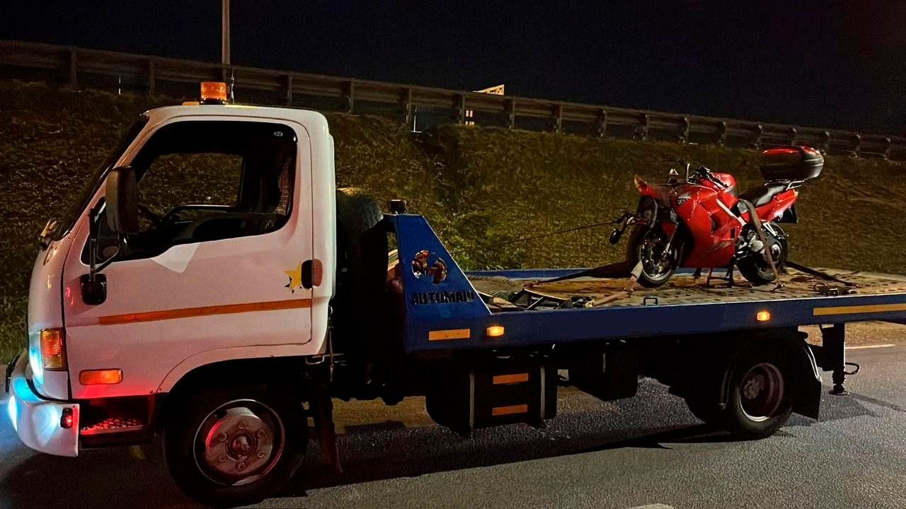 Tow truck transporting a red motorcycle at night on a roadway with barriers in the background.