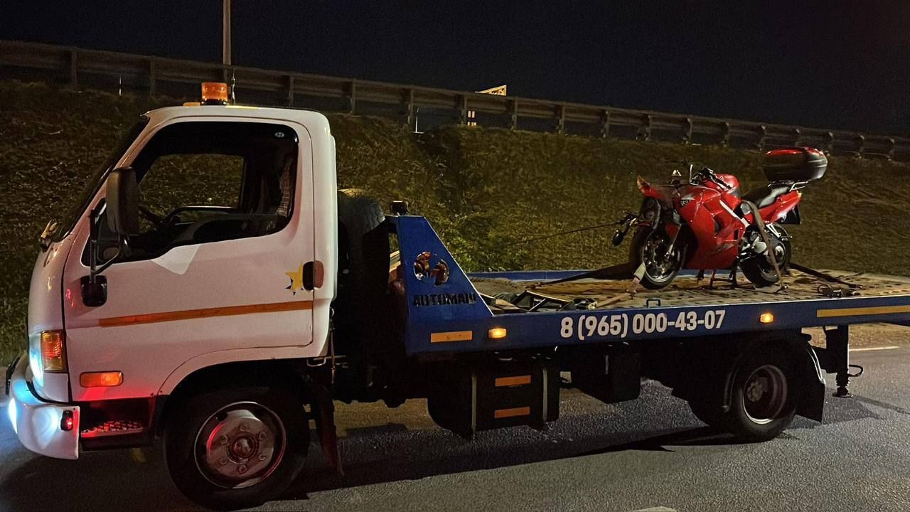 Tow truck carrying a red motorcycle on a flatbed at night.