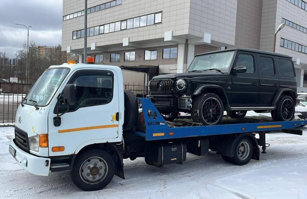 Tow truck transporting a black SUV in front of a multi-story building on a snowy day.