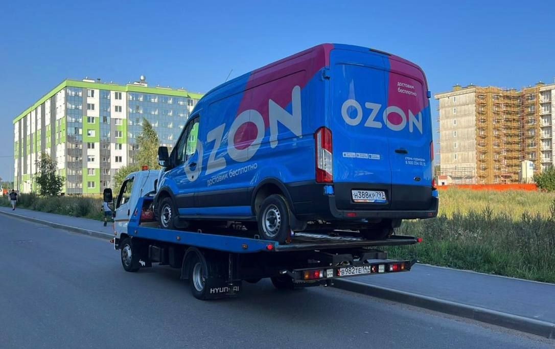 Blue delivery van on a tow truck in front of an apartment building with green accents.