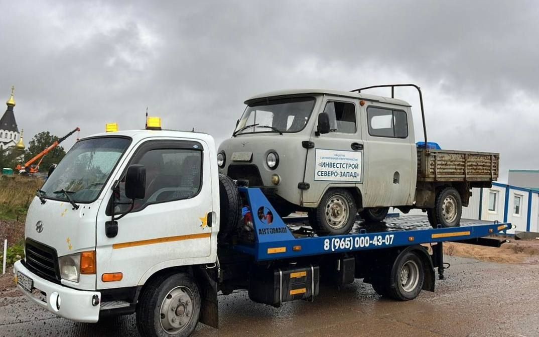 Tow truck carrying an old van under cloudy skies near a construction site.
